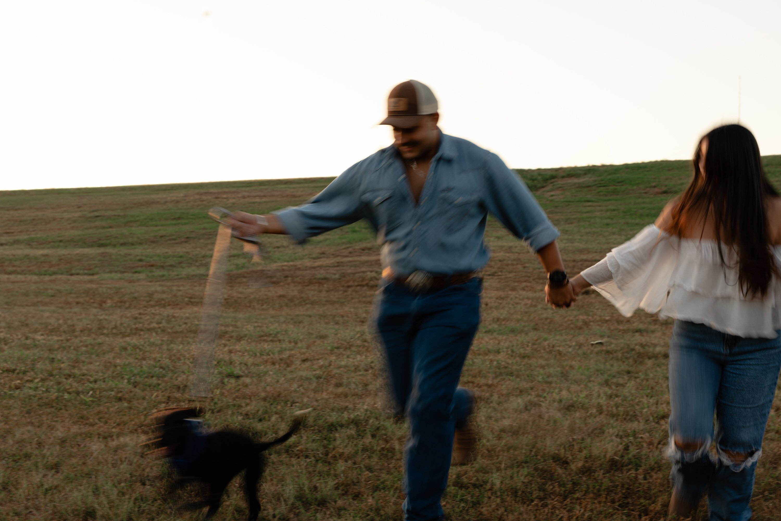 Engaged couple running hand in hand through a golden field