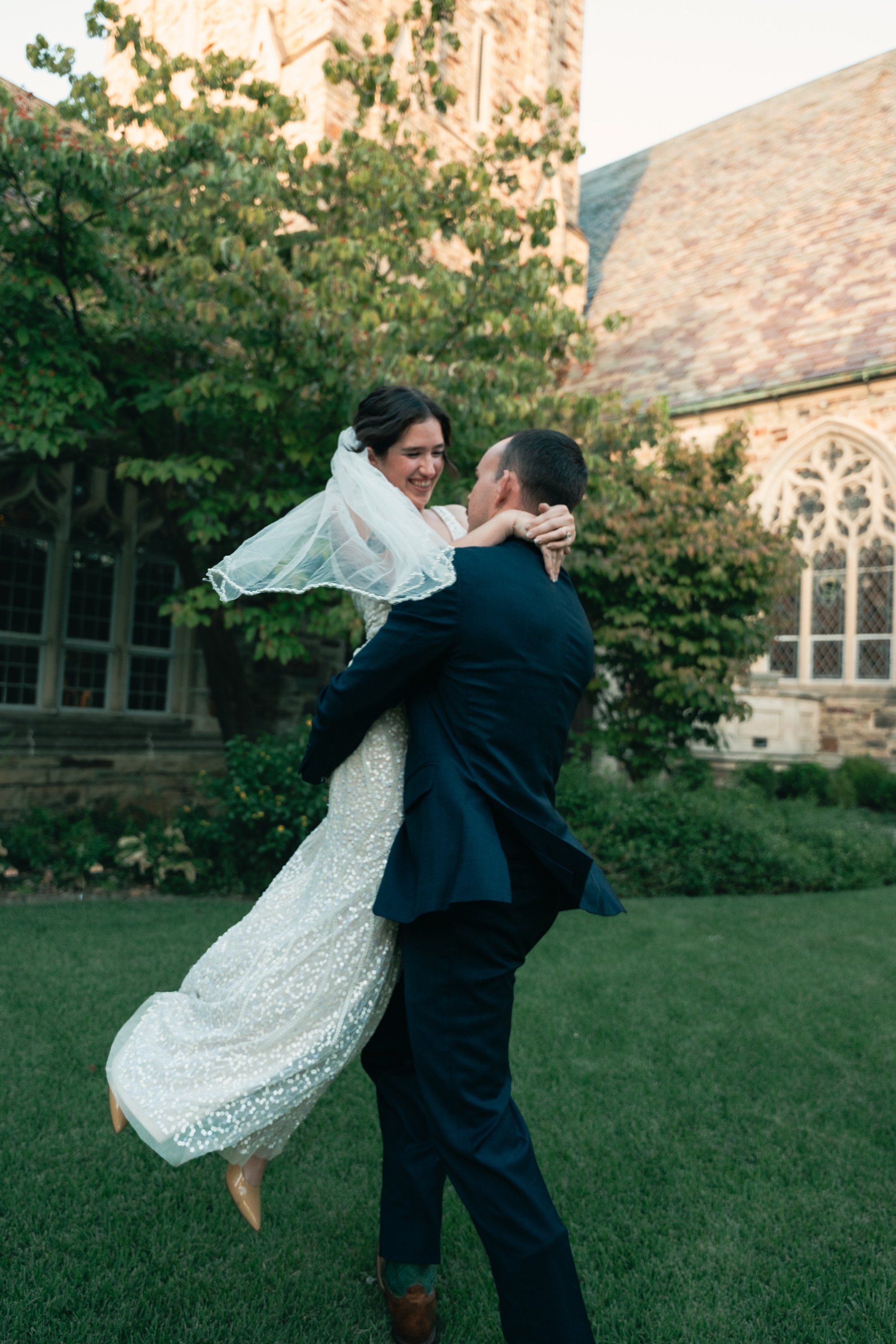 Groom lifting his laughing bride, her veil flying