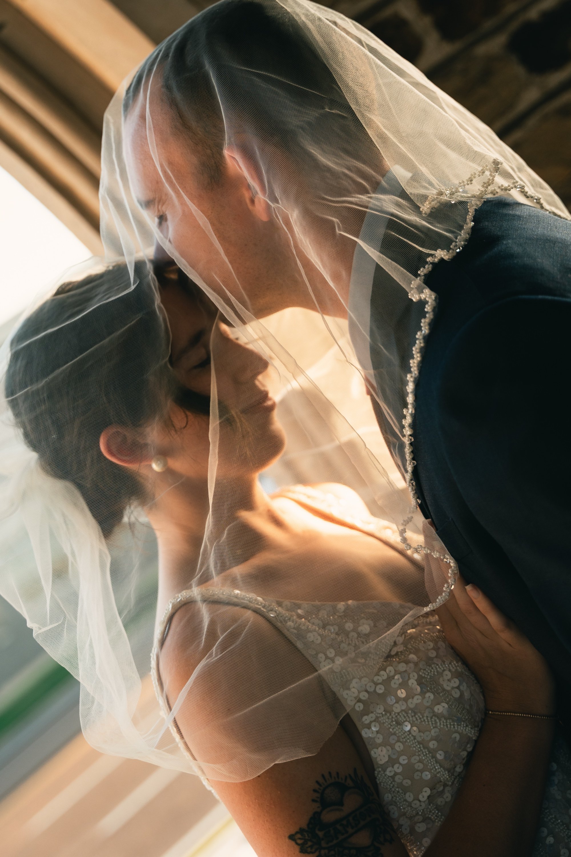 Groom kissing the bride beneath her veil in golden light, romantic wedding photography by a Memphis wedding photographer