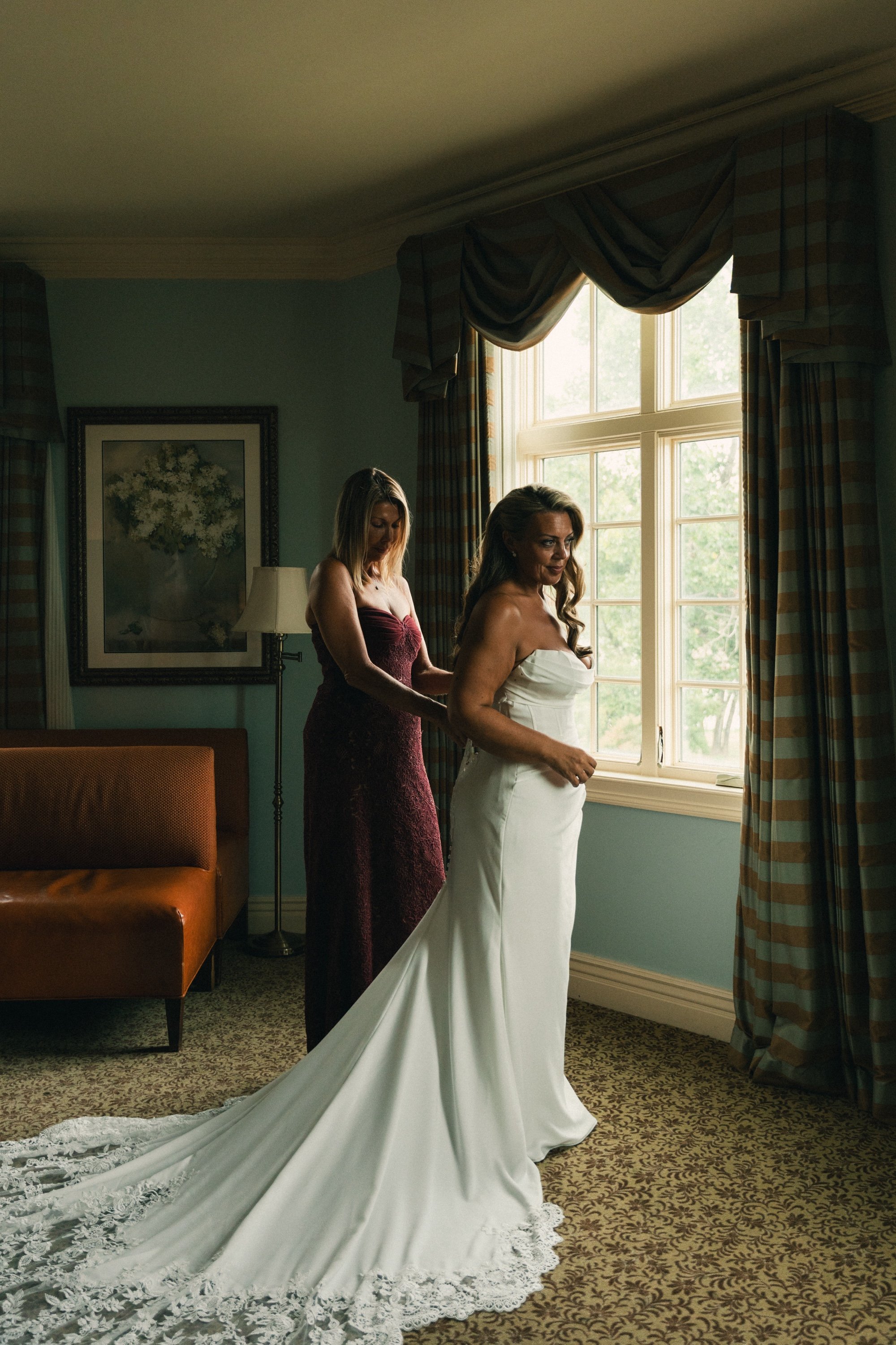The bride's gown being buttoned beside a tall window